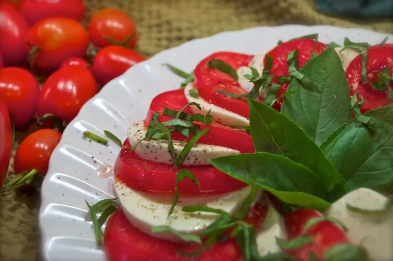 Fresh tomato mozzarella salad with basil, olive oil, and balsamic glaze on a white serving plate