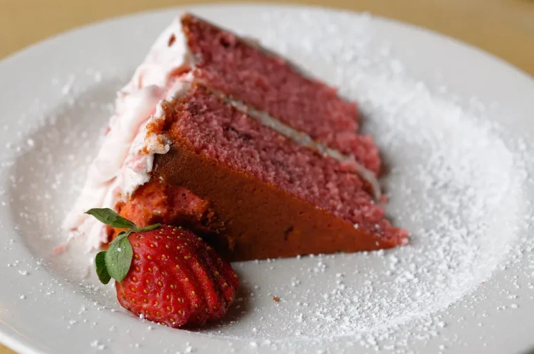 Slice of moist Southern strawberry cake with pink frosting on a white plate