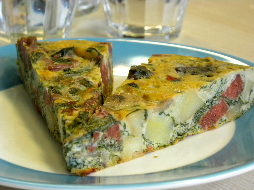 Slice of oven-baked frittata topped with herbs on a breakfast table.
