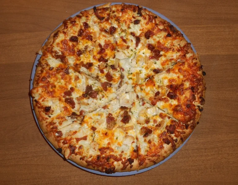 Close-up of cheesy chicken bacon ranch pizza slices topped with ranch dressing and fresh parsley.