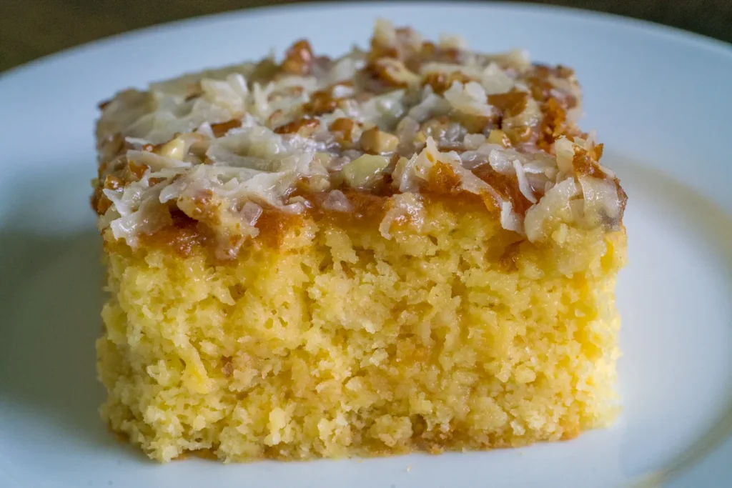 Slice of classic Do Nothing Cake with cream cheese frosting and shredded coconut on top