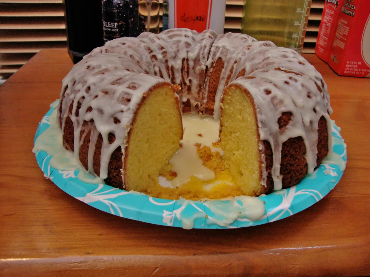 Sliced sugar-free lemon cake with iced glaze drizzled on top, served on a wooden board