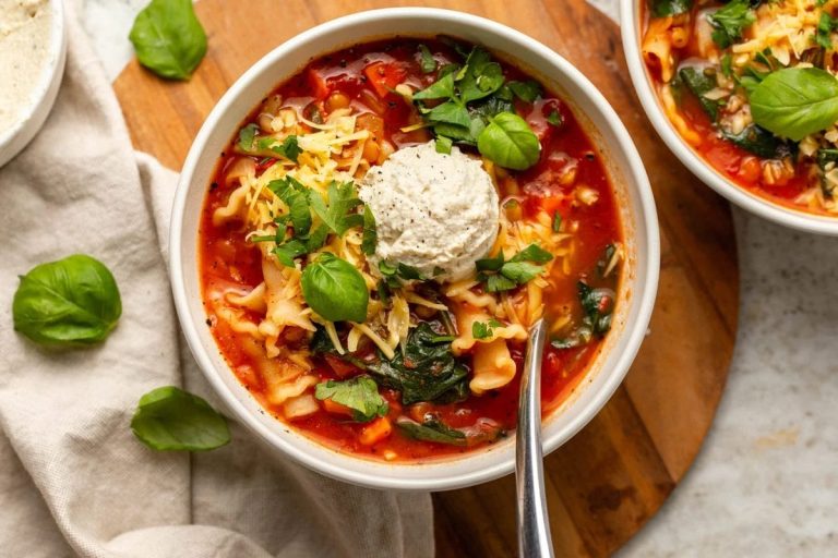 Hearty lasagna soup with broken noodles, ground beef, and ricotta cheese, garnished with parsley and served with bread.