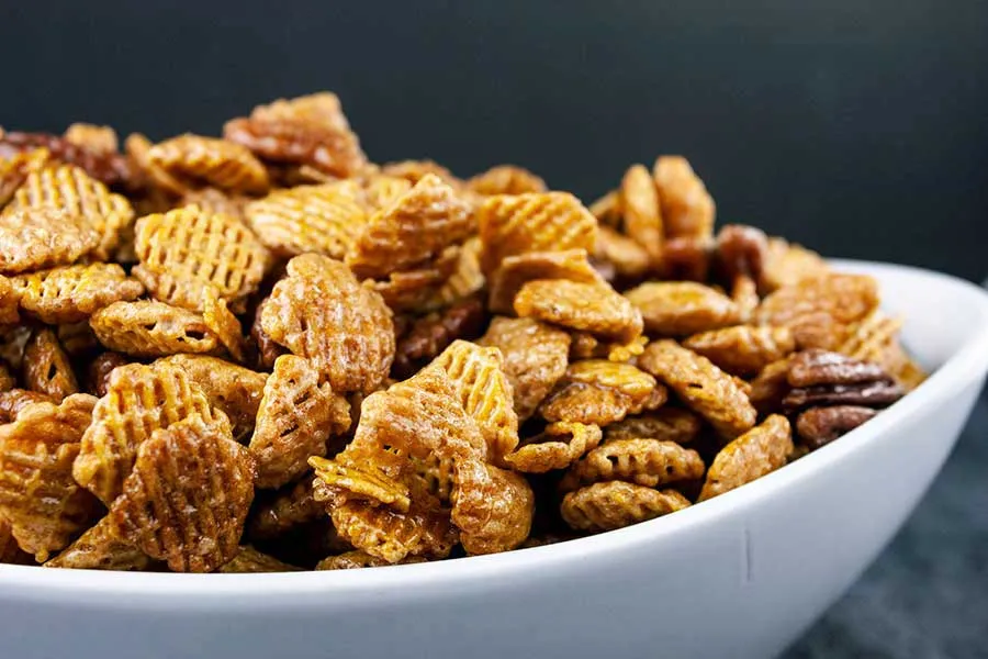 Homemade praline crunch snack mix with caramel-coated cereal and toasted pecans on a baking sheet.