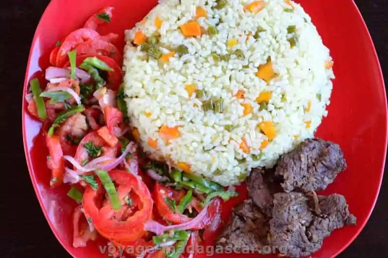 Healthy rice salad bowl with colorful vegetables and fresh herbs on a white plate.
