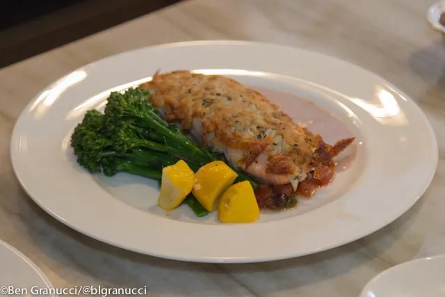 Pan-seared branzino fillet with crispy golden skin, served with lemon butter sauce and fresh herbs on a white plate.