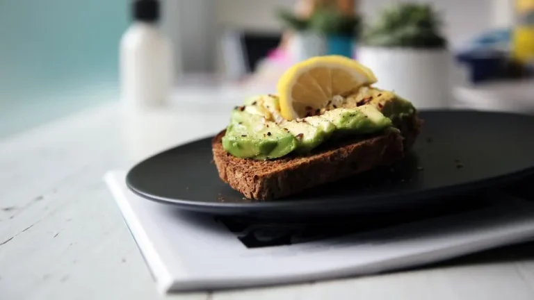 Close-up of a golden sourdough breakfast sandwich with eggs, cheese, and avocado, surrounded by fresh fruits and coffee.