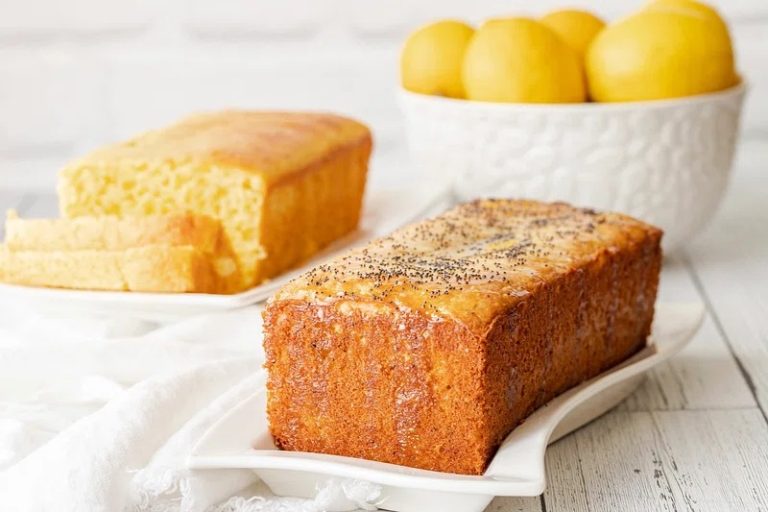 Freshly baked lemon cake with zest and glaze, surrounded by sliced lemons.