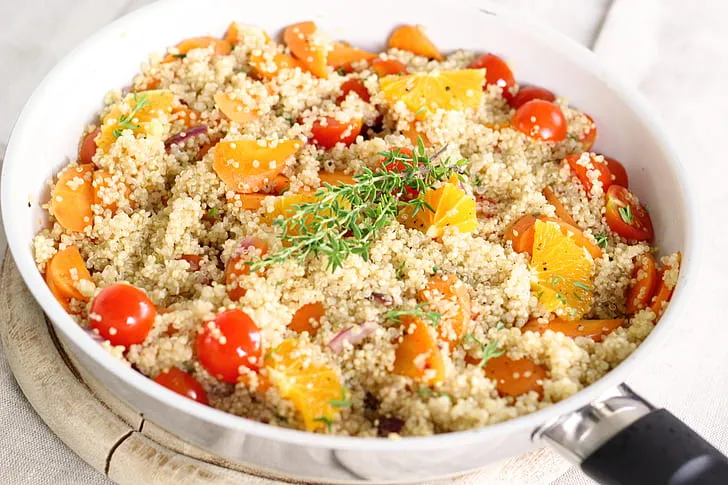 Fresh quinoa salad with cherry tomatoes, cucumber, and chickpeas served in a white bowl on a wooden table, topped with herbs and lemon dressing.