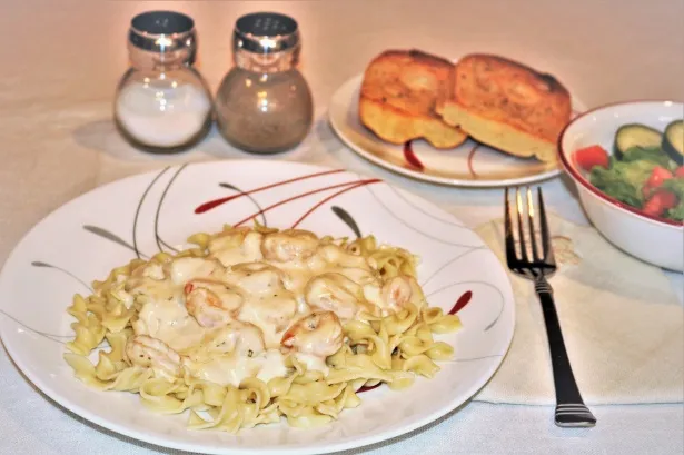 Close-up of creamy Cajun Alfredo sauce on pasta with shrimp and chicken, sprinkled with parsley and Parmesan.