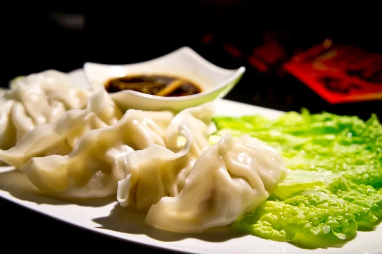 A plate of freshly cooked dumplings with dipping sauce, golden and ready to eat.