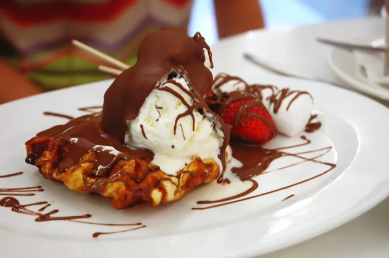 Stack of homemade Belgian waffles on a plate with syrup drizzle and a cup of coffee in the background.