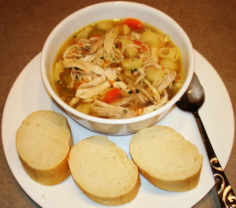 Comforting classic chicken noodle soup served with fresh herbs and bread on a rustic kitchen table.