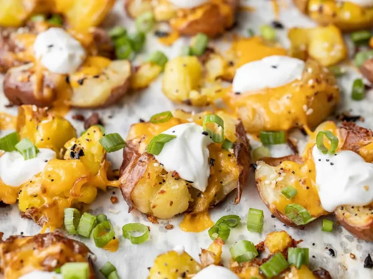 Golden baked smashed potatoes on a tray with cheddar, bacon, and fresh herbs
