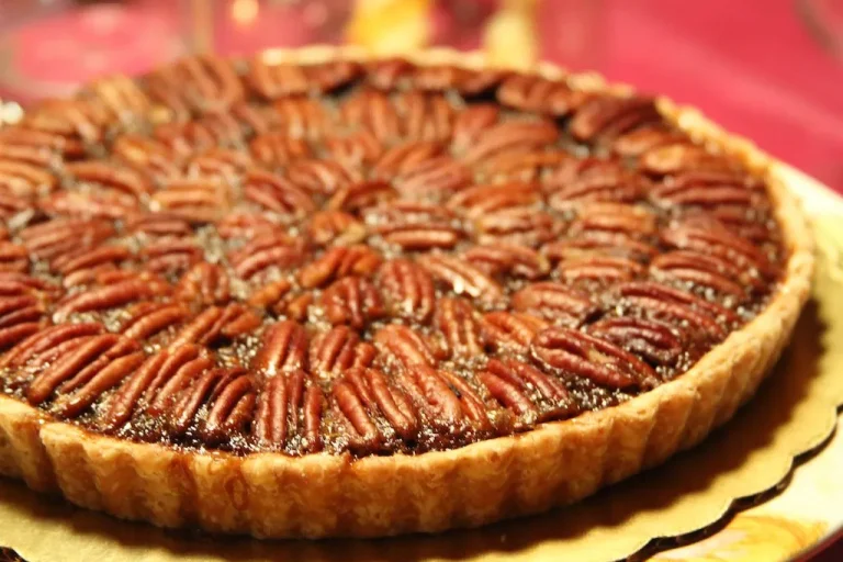 Slice of homemade pecan pie served with whipped cream and toasted pecans.