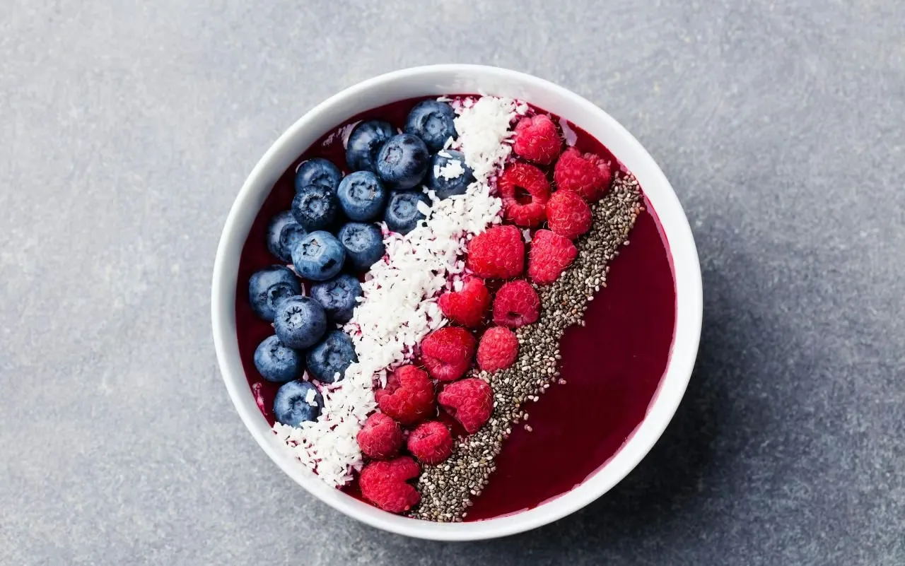 A thick, vibrant açaí bowl topped with fresh berries, banana slices, granola, and chia seeds