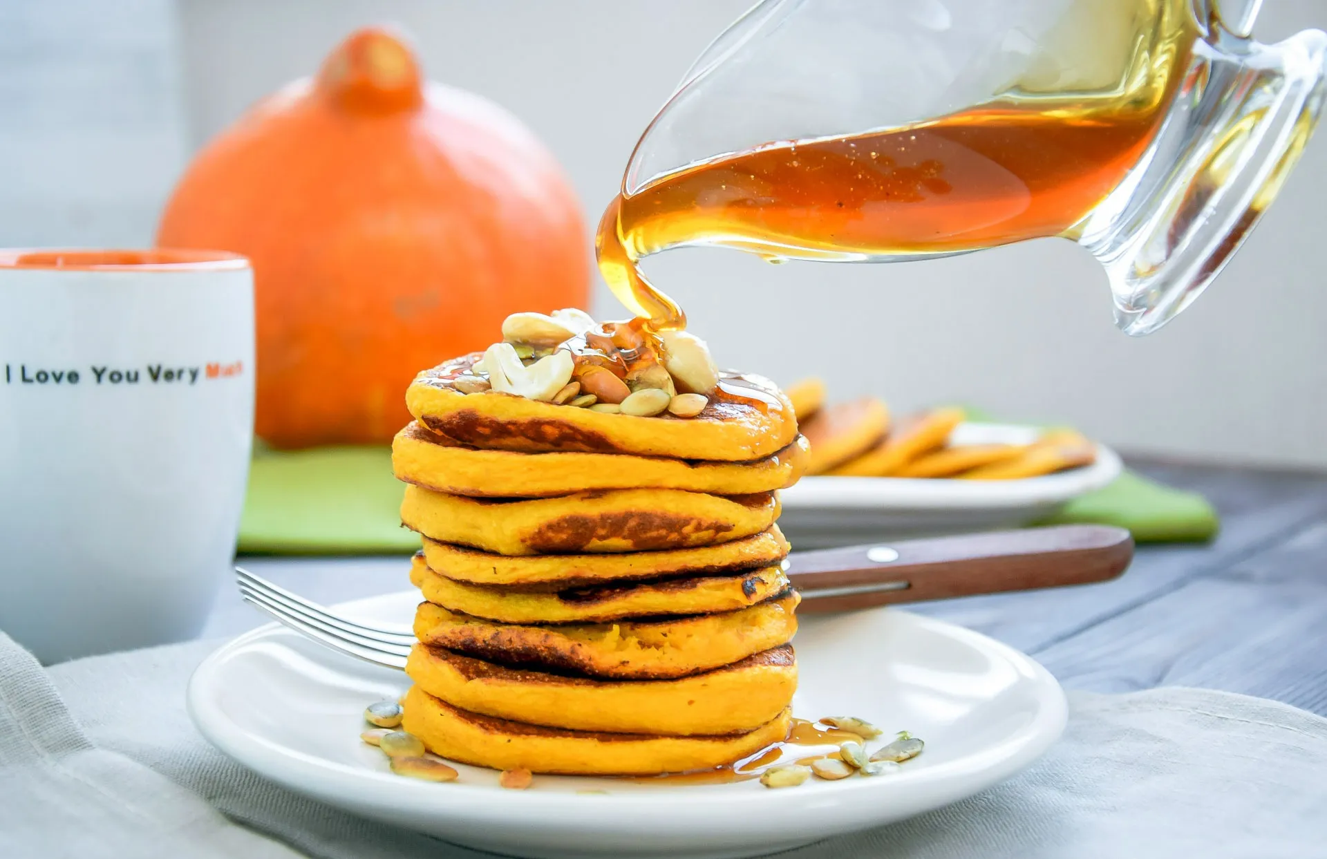 Stack of fluffy pumpkin pancakes topped with maple syrup and cinnamon on a cozy fall breakfast table.